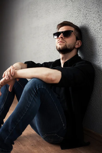 Hombre joven en camisa sentado con las manos apretadas contra una pared —  Fotos de Stock