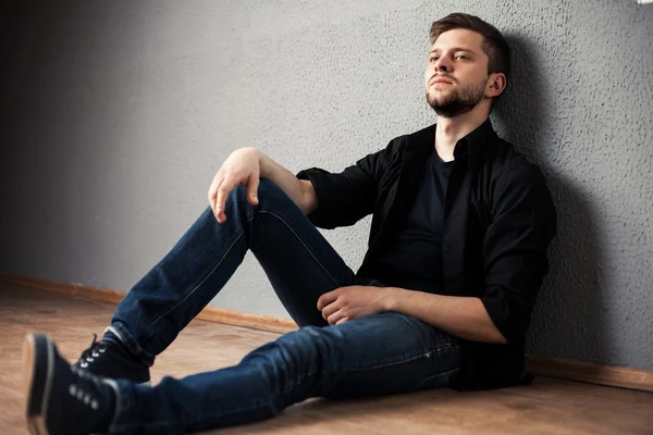 Young man in shirt siting with hands clasped against a wall — Stock Photo, Image