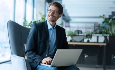 Businessman using laptop computer in office. Happy middle aged man, entrepreneur, small business owner working online