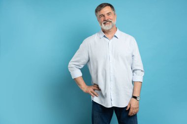 Mutlu, sıradan, gülümseyen yaşlı bir adamın portresi, orta yaşlı, gri saçlı, mavi arka planda izole edilmiş, kopyalama alanı olan yetişkin bir erkek.