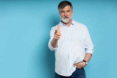 Seni seçiyorum ve emir veriyorum. Gülümseyen iş adamı seni işaret ediyor, seni istiyor, mavi stüdyo arka planında yarım boy yakın plan portre. İnsani duygular, yüz ifadesi kavramı. Ön görünüm