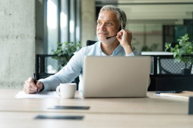 Gülümseyen işadamı müşteriyle konuşurken kulaklık kullanıyor. Kulaklıktaki teknik destek müdürü bir müşteriye danışıyor. Ofiste çalışan olgun erkek müşteri desteği yöneticisi..