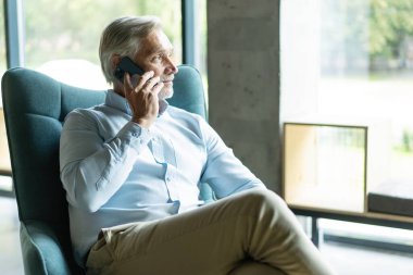 Akıllı telefonlu bir iş adamı ofisinden cep telefonuyla arıyor. Beyaz adam ofis lobisinde oturuyor. Arama yapmak için cep telefonu kullanıyor.