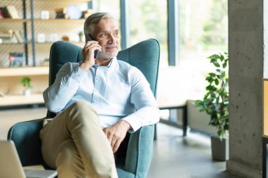 Akıllı telefonlu bir iş adamı ofisinden cep telefonuyla arıyor. Beyaz adam ofis lobisinde oturuyor. Arama yapmak için cep telefonu kullanıyor.