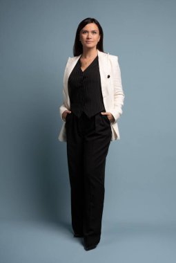 Güzel, çekici, orta yaşlı, sıradan beyaz ceket giyen, mavi arka planda tek başına duran bir kadın. Kendine güvenen başarılı kadın kameraya bakıyor. İş konsepti