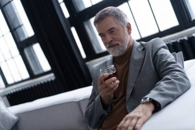 Kendine güvenen olgun iş adamı rahatlıyor işten sonra viskinin tadını çıkarıyor.