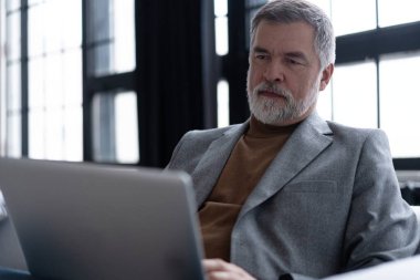 Melez işi, e-öğrenme, online öğrenme. Mutlu gülümseyen olgun bir adam dizüstü bilgisayara bakıyor. Kanepede oturmuş Webinar izliyor.