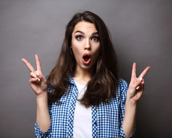 Porträt einer glücklichen Frau, die den Sieg mit den Fingern über dem grauen Hintergrund zeigt und in die Kamera blickt — Stockfoto