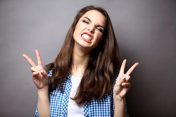 Portret van een gelukkige vrouw tonen overwinning met vingers op grijze achtergrond en kijkend naar camera — Stockfoto