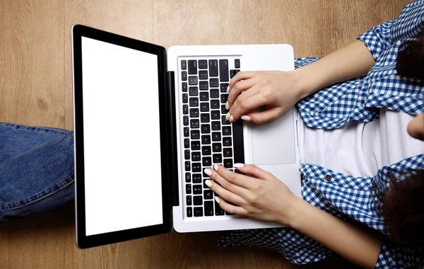 Laptop in Mädchenhänden tippt und sitzt auf einem Holzboden — Stockfoto