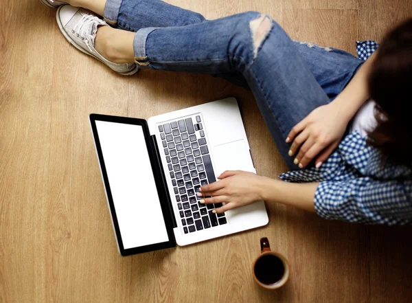 Laptop in girls hands typing and sitting on a wooden floor — Stock Photo, Image
