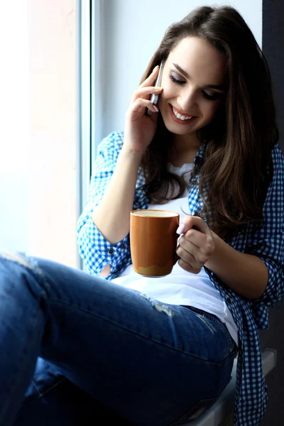 Pretty peaceful young woman using cell phone and drinking coffee — Stock Photo, Image