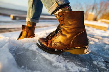 Kış geliyor. Pürüzlü buz yüzeyinde kadın botları. Kahverengi deri ayakkabılı bir kadın kaygan buz merdiveninden iniyor.