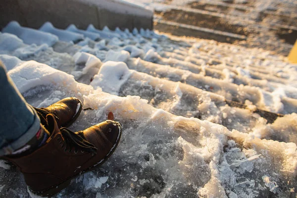 Pericolo di scivolamento. Stivali femminili su una superficie di ghiaccio ruvida. Una donna in scarpe di pelle marrone scende la scivolosa scala di ghiaccio — Foto Stock