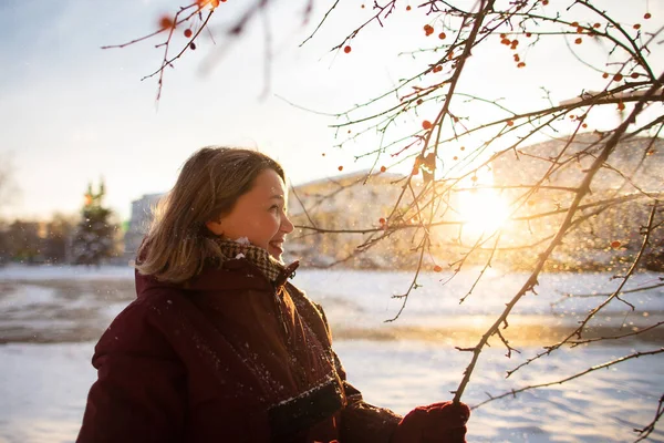 Activités hivernales saisonnières. Belle femme jetant de la neige dans les airs au coucher du soleil en tenant des branches d'arbres — Photo