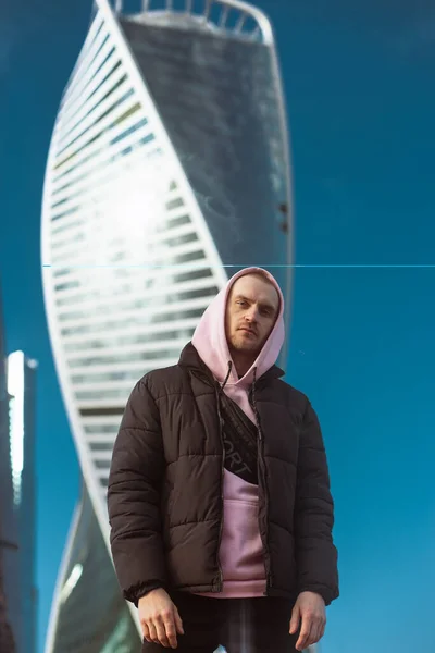 Bonito homem casual em casaco preto e rosa com capuz em pé em uma vista arranha-céu — Fotografia de Stock