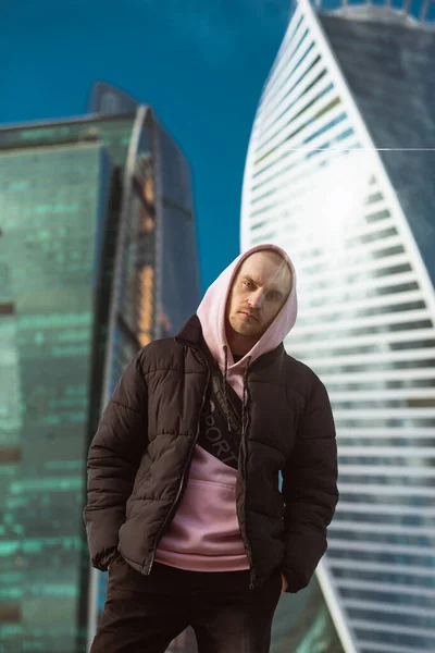 Bonito homem casual em casaco preto e rosa com capuz em pé em uma vista arranha-céu — Fotografia de Stock