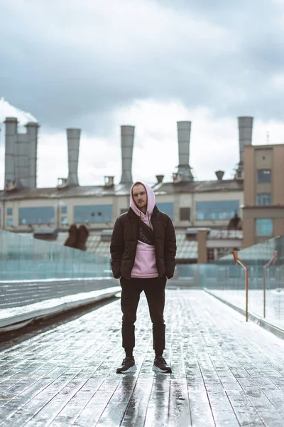 Bonito homem casual em windbreaker de pé sobre a ponte subindo fundo industrial — Fotografia de Stock