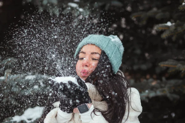 Winter fun, holidays and people concept - brunette woman in blue winter hat blowing snow from her gloves — Stock Photo, Image