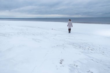 Kaçış, doğa rahatlama konsepti. Kış denizinin arka planında ceketli yalnız bir kız. Denizdeki bir kadının portresi, rüzgarlı hava, soğuk atmosferik görüntü.