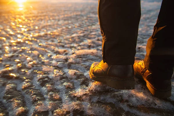 Winter is coming. Female boots on rough slipper ice surface. A woman in brown leather shoes walking on winter sea coastline