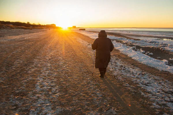 冬季运动在北方人的步行.老年妇女在冬季海滨徒步旅行.活跃的人们在户外。宁静的日落风景 — 图库照片