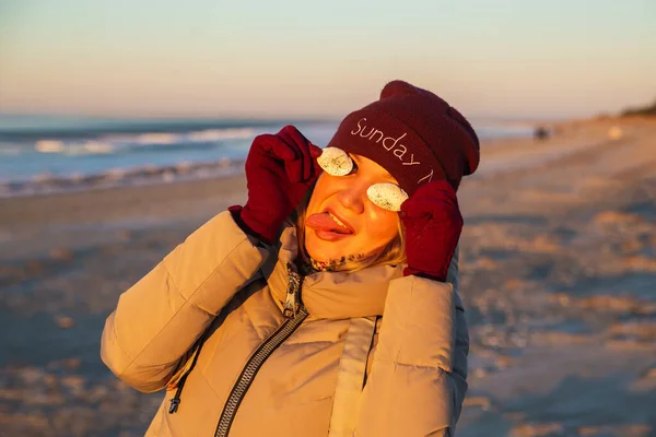 Deniz kabuklu güzel bir kadın güneşli bir kış gününde deniz kıyısında eğleniyor. — Stok fotoğraf