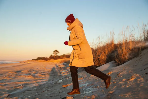 Красива біла жінка в зимовому одязі біжить на берегову лінію на тлі зимового моря. Розмивання руху. Ескапізм, гармонія з природою — стокове фото
