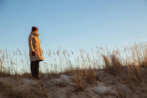 Красивая кавказка в зимней одежде, смотрящая на солнце на фоне зимней замерзшей травы. Портрет женщины на природе, солнечная ветреная погода, атмосферный образ. Бегство, гармония — стоковое фото