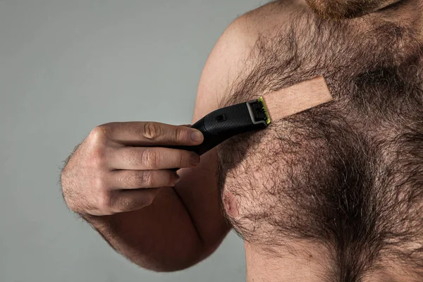 Yakışıklı kıllı adam kıllı göğsünü budayarak tıraş ediyor. Testosteron ve tıraş konsepti.