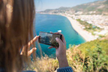 Bir blogcu plajda tatilcilerle ve denizde yüzen insanlarla bir video çekiyor.