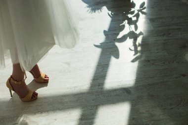 Gelinlerin bacakları gür bir elbise içinde ve çıplak ayakla güneş ışığındaki çiçeklerin gölgesinde