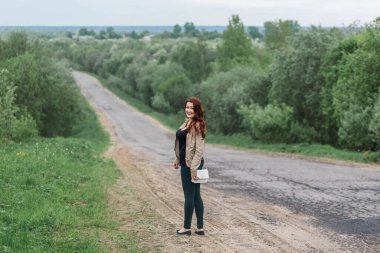 Boş asfalt yolda yürüyen genç bir kadın. Kameraya bakan mutlu kız