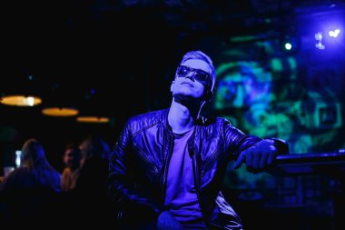 Deri ceketli, güneş gözlüklü ve neon ışıklı yakışıklı bir adam.