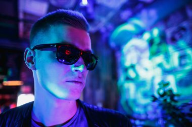 Deri ceketli, güneş gözlüklü ve neon ışıklı yakışıklı bir adam.