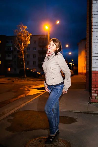 Красивая молодая девушка в джинсах и бежевой куртке позирует в типичном русском городке — стоковое фото