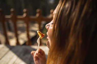 Bir kız yaz verandasında çatalla yemek yiyor.