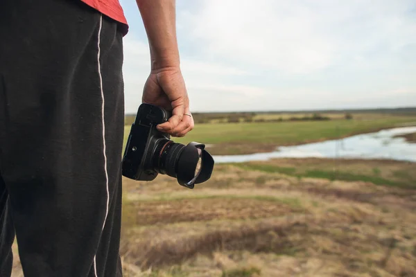 Мужчина-фотограф-любитель с камерой стоит на холме возле зеленого луга на закате. Фотограф-ландшафт — стоковое фото