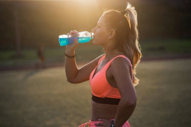 Eğitimden sonra bir kadın su içiyor. Genç ve gülümseyen bir kız fiziksel yorgunluktan sonra izotonik bir içki içiyor. Kadın elinde mavi bir sıvıyla bir şişe tutuyor. Sağlıklı yaşam tarzı kavramı