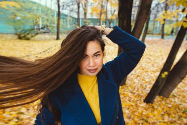 Elinde sonbahar yaprakları olan ve sarı akçaağaç bahçesinden düşen neşeli genç bir kadın.