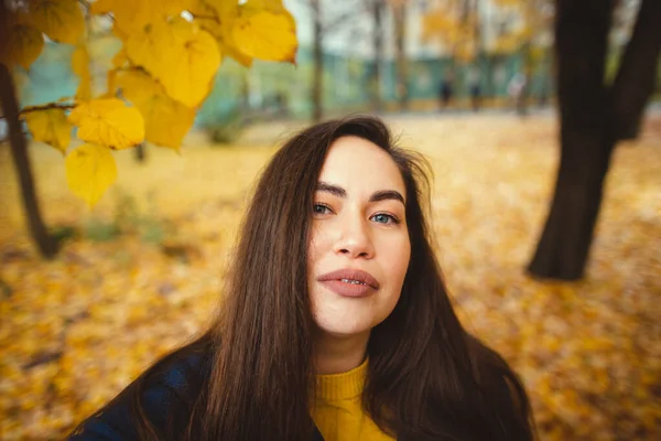 一个快乐的年轻女子，手里拿着秋天的叶子，落在了黄色的枫树花园背景上 — 图库照片