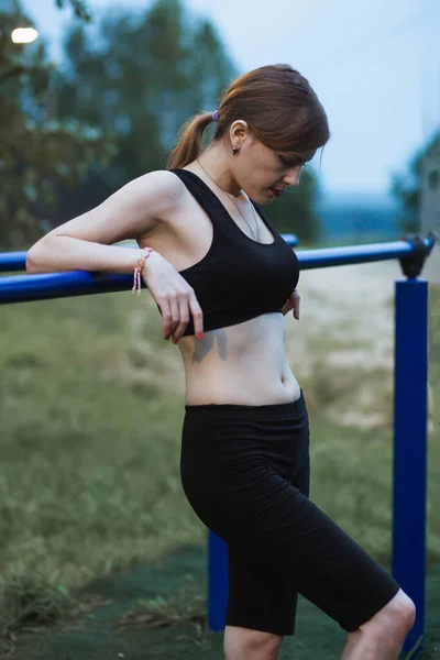Mladá krásná dívka dělá chin-ups na venkovním sportovišti. Večerní pouliční cvičení — Stock fotografie