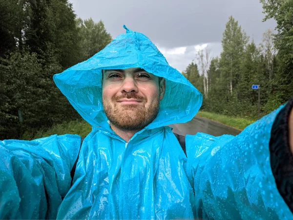 Ein Mann im blauen Regenmantel fotografiert mit dem Smartphone im herbstlichen Regenwald — Stockfoto