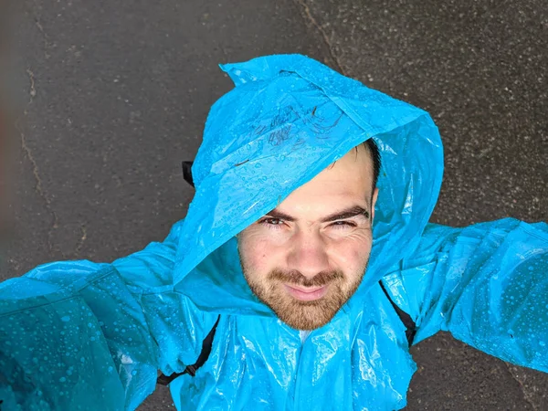 Мужчина в синем плаще фотографируется со смартфоном в осеннем дождевом лесу — стоковое фото