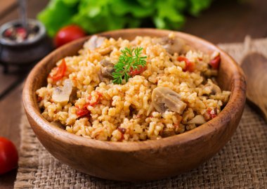 Bulgur with chicken, mushrooms and tomatoes in a wooden bowl. clipart