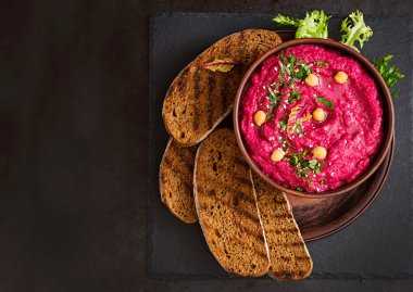 Kavrulmuş pancar Humus ile karanlık bir arka plan üzerinde seramik bir kasede tost
