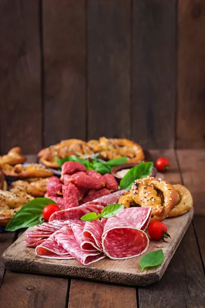 Pretzels and various sausages on wooden table — Stock Photo, Image