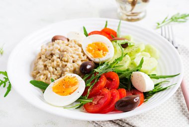 Kahvaltı yulaf lapası, Yunan salatası, salatalık, zeytin ve yumurta. Sağlıklı dengeli yiyecekler.