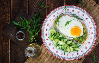 Sağlıklı kahvaltı. Noel brunch 'ı. Avokado sandviçi, sahanda yumurta ve ahşap masada roka ile salatalık. Üst görünüm, alanı kopyala