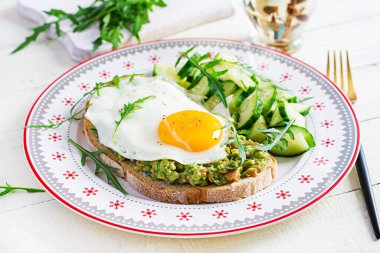 Sağlıklı kahvaltı. Noel brunch 'ı. Yağda yumurtalı avokado sandviçi ve sağlıklı kahvaltı için roka ve taze salatalıklı salata..